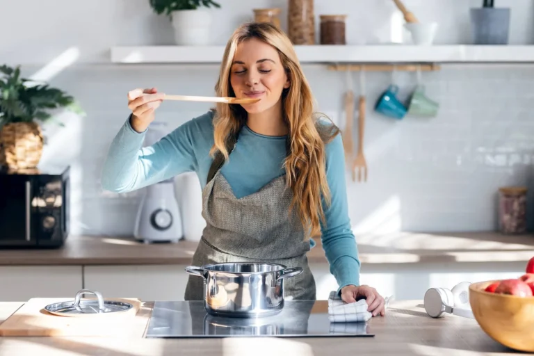 Dietary Deficits: Are Nutrient Gaps Draining You? Woman cooking healthy food in casserole while blowing the spoon to taste the food