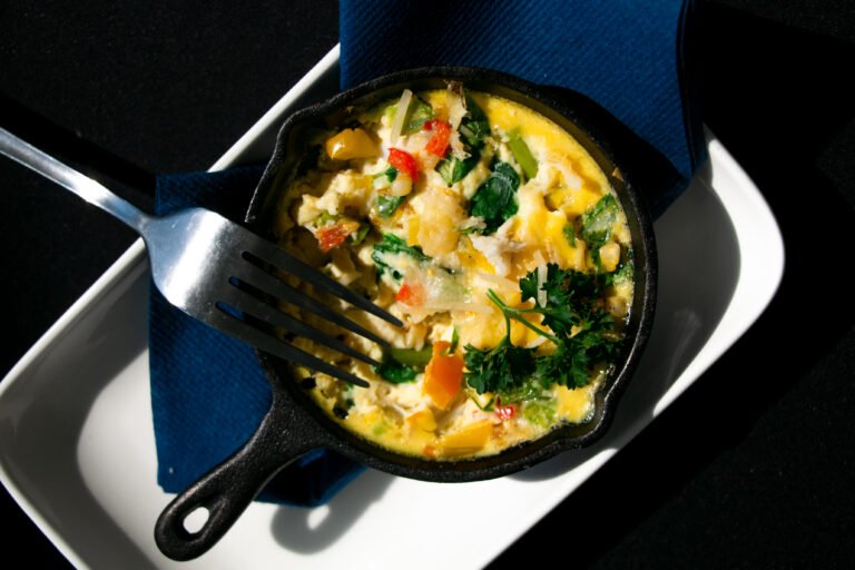 A cooked egg frittata with colorful vegetables sits in a small black cast iron and serving dish after being tasted by the judges.