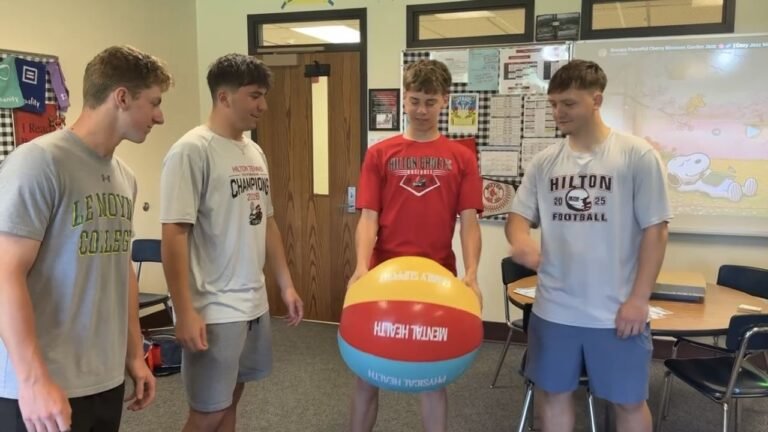 Four Hilton High School students participate in a color wheel exercise, with one holding a beach ball